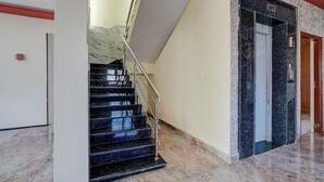 A modern interior with a marble staircase, a lift, and a hallway with a red accent wall. - Via Aero Nest (Bengaluru)
