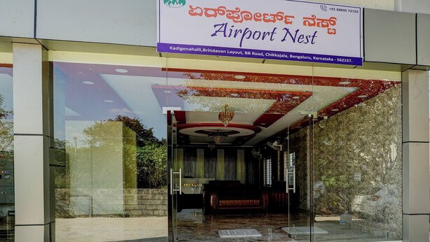 The entrance of a hotel named 'Airport Nest' with a glass facade and a red and gold interior design. - Via Aero Nest (Bengaluru)