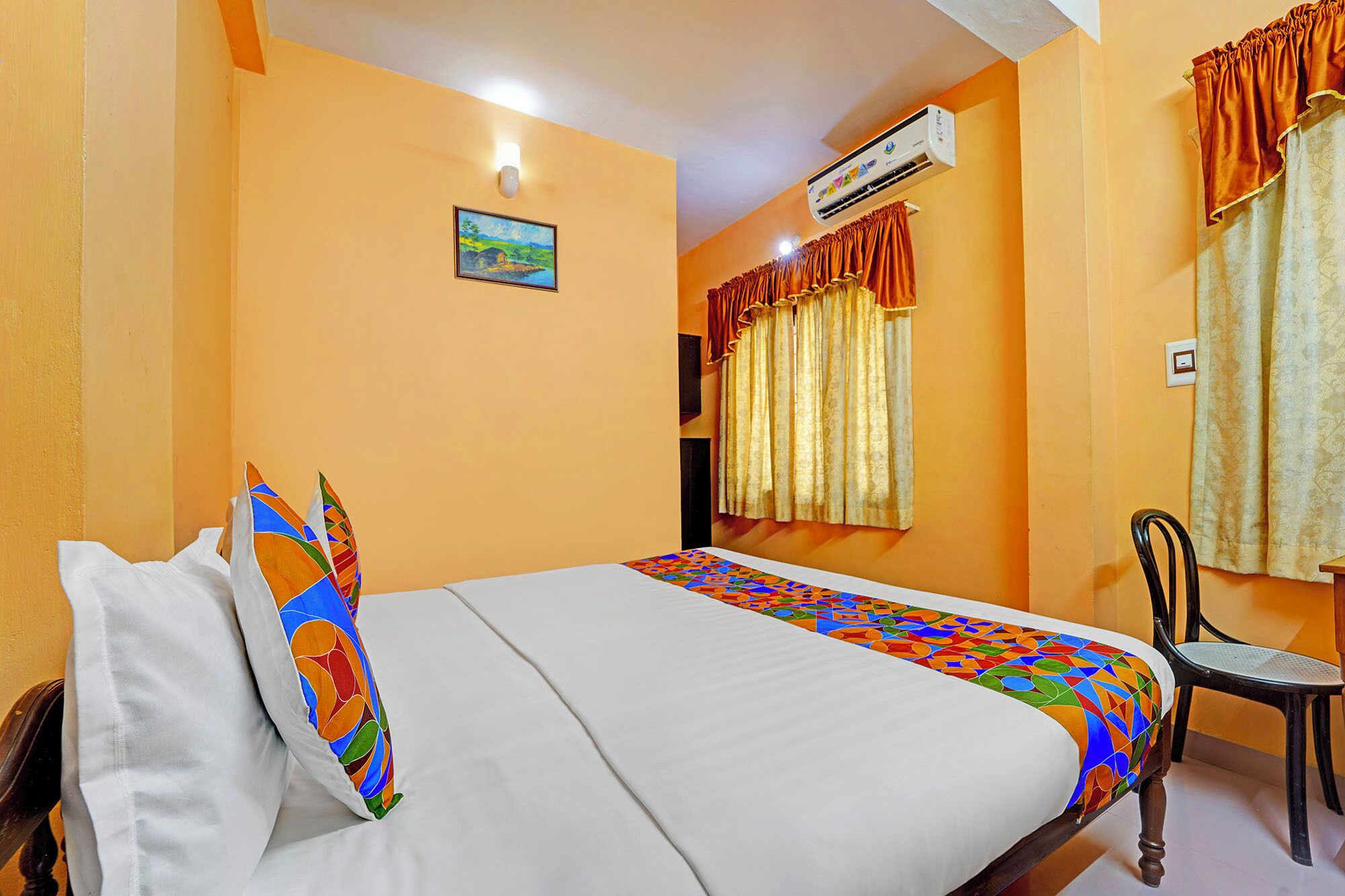 Quarto de hotel com cama, cadeira, ar condicionado e um quadro na parede.