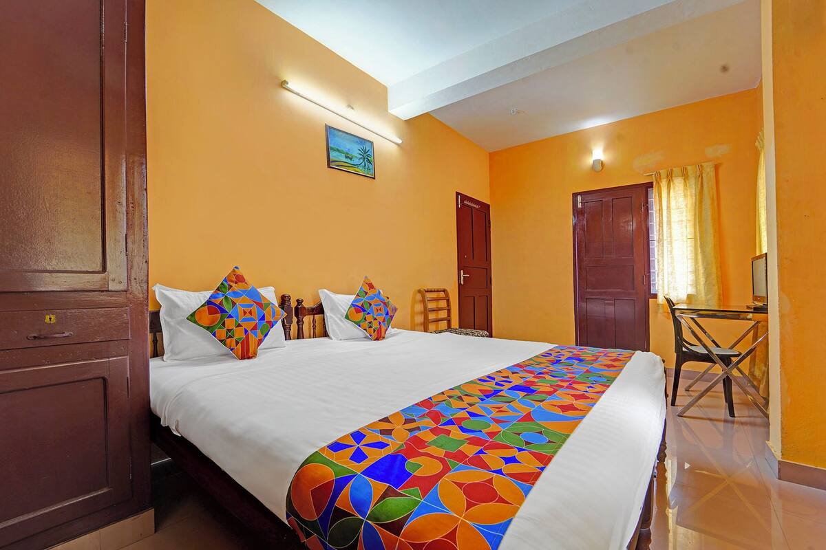 A hotel room with a bed, two pillows, a chair, a desk, and a door.