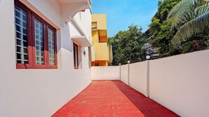A narrow, red-tiled corridor with white walls and a white fence, leading to a building with multiple windows and balconies. - Via Fort Beach Residency (Kochi)