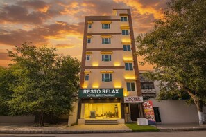Un hotel de varios pisos llamado Resto Relax, con un diseño moderno, que presenta una entrada destacada y un cartel anunciando el hotel.