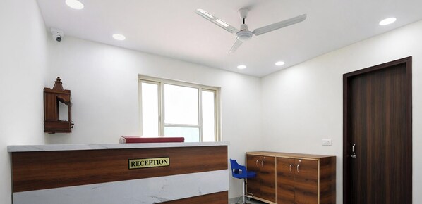 Zona de recepción con un mostrador de madera que dice "RECEPTION", una ventana, un ventilador de techo y un armario de madera.