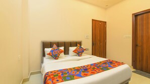 A hotel room with a bed, two pillows, a wooden door, and a light switch on the wall. - Fabhotel Kesar Inn (Jaipur)