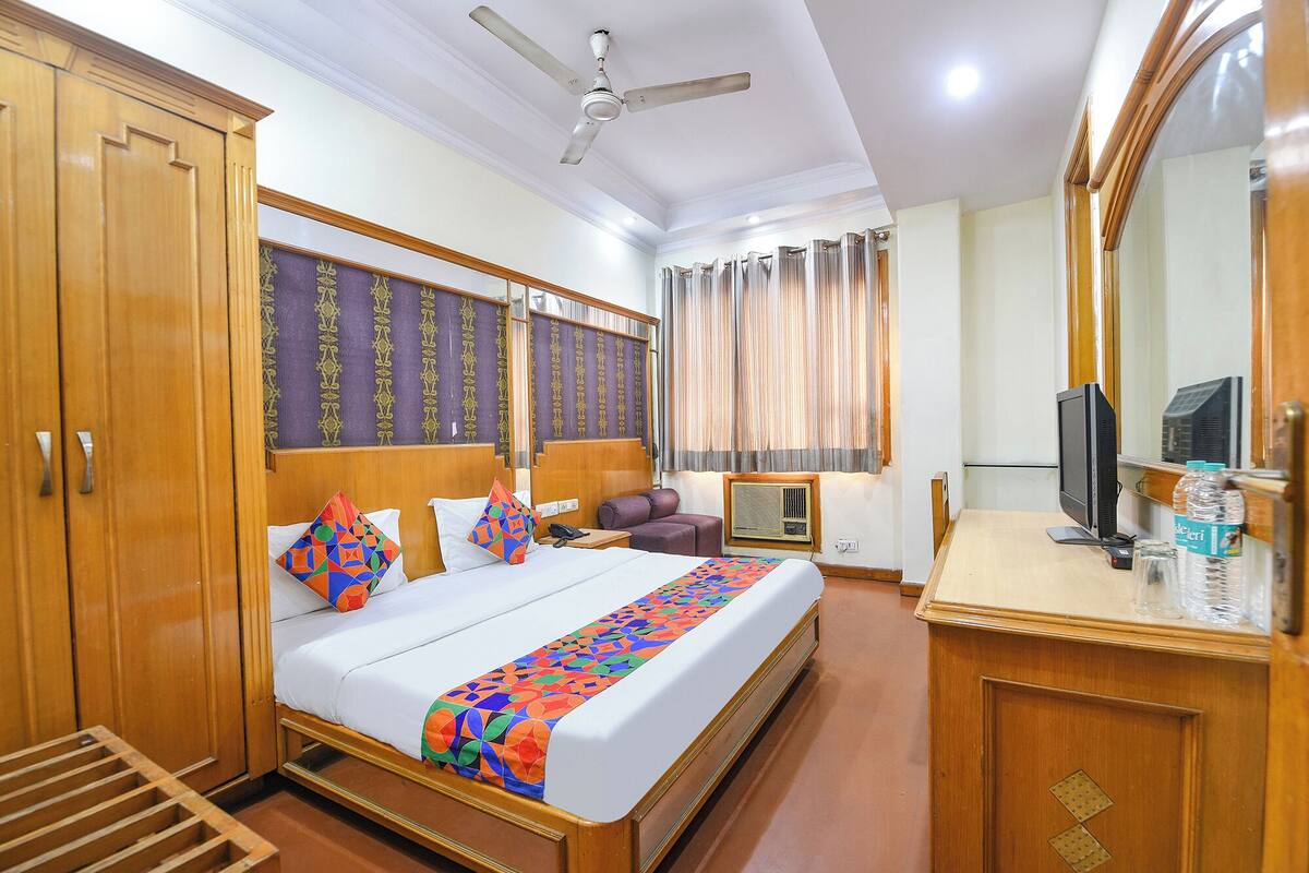 A hotel room with a large bed, a desk with a computer, a wardrobe, a ceiling fan, and a window with curtains.