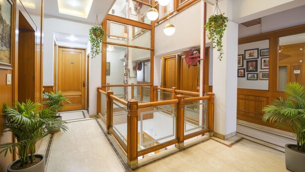 A hotel lobby with a wooden reception desk, a glass partition, and potted plants. - Fabhotel Kochar Continental (New Delhi)