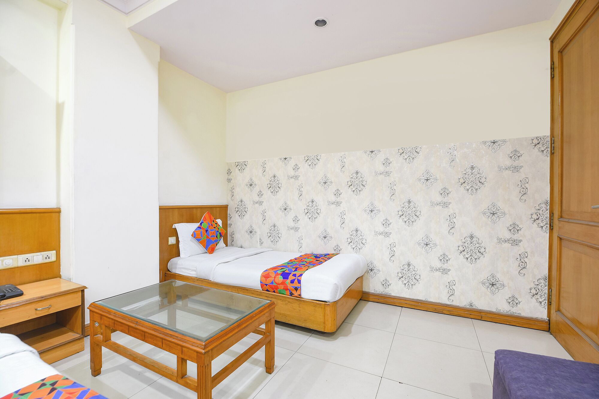 A room with a bed, a glass-top table, a wooden nightstand, and a wardrobe.