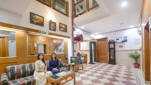 A lobby with a checkered floor, wooden furniture, a sofa, a coffee table, a clock, and a television. - Fabhotel Kochar Continental (New Delhi)