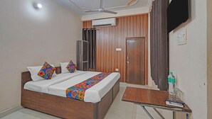 Une chambre à coucher comprenant un lit, un ventilateur de plafond, un appareil de climatisation, une armoire en bois, une porte, une petite table avec une bouteille et des verres, et un téléviseur fixé au mur.