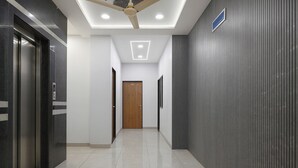 A modern hallway with a ceiling fan, recessed lighting, a wooden door at the end, and a textured wall on the right. - Fabhotel Kavish Villa (Indore)