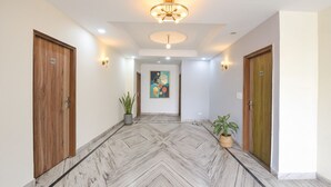 A hallway with a marble floor, wooden doors, and wall-mounted light fixtures. - Via Esscon House (Gurugram)