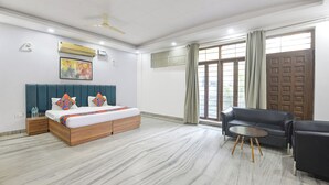 A hotel room with a bed, a sofa, a small table, and a window with curtains. - Via Esscon House (Gurugram)