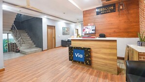 A reception area with a wooden reception desk, a staircase, and a 'Via' sign. - Via Esscon House (Gurugram)