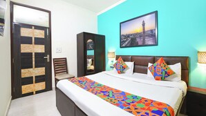 A hotel room with a bed, a view of a cityscape, a door with a geometric pattern, and a nightstand with a lamp. - Via KD6 Plaza Residency (New Delhi)