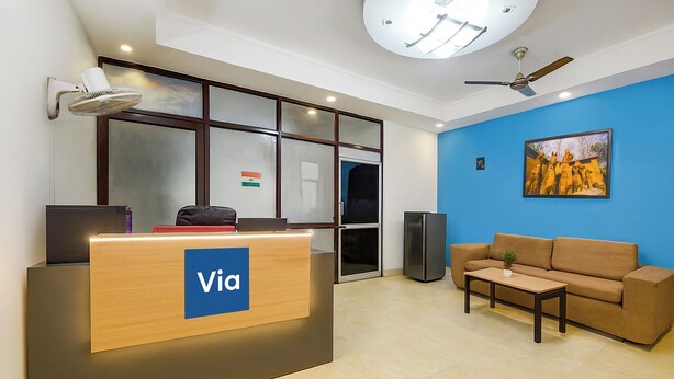 A reception desk with a 'Via' sign, a blue wall, a brown sofa, a ceiling fan, and a painting. - Via KD6 Plaza Residency (New Delhi)