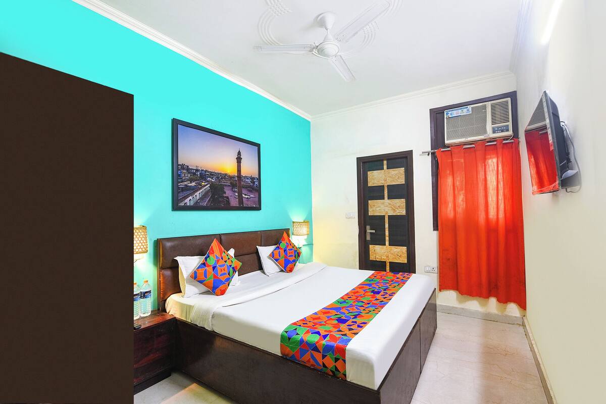 A bedroom with a bed, a ceiling fan, a picture on the wall, and an air conditioning unit.