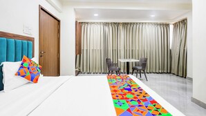 Een hotelkamer met een bed, een kleintje tafeltje, twee stoelen en een raam met gordijnen.