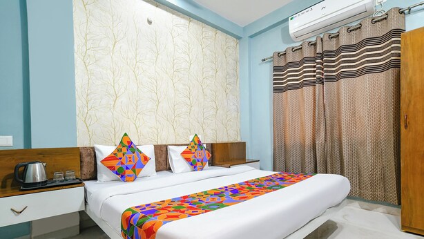 A hotel room with a bed, a nightstand, a kettle, and a red chair. - Via Kanha Palace (Ujjain)