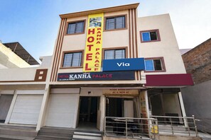 A hotel named 'Kanha Palace' with a yellow sign, a blue sign indicating a nearby road, and a closed front door. - Via Kanha Palace (Ujjain)