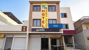 A hotel with a prominent yellow sign, a blue sign indicating a nearby road, and a staircase leading to the entrance. - Via Kanha Palace (Ujjain)