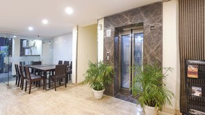 En moderne hotellobby med et marmorgulv, et spiseområde med glasvæg og en receptionsdisk med elevator.