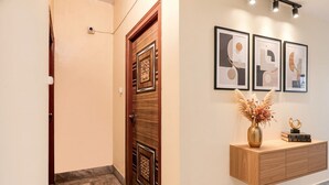 Um corredor com porta de madeira, chão de mármore e um armário fixado na parede, com um vaso e livros.