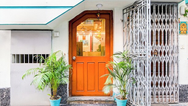 Uma casa com porta de madeira, portão de metal e dois vasos de plantas.