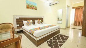 A hotel room with a bed, a chair, a rug, a painting, and an air conditioning unit. - Fabhotel The Glory (Rishikesh)