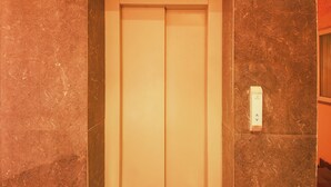 A closed elevator door with a marble wall and a light switch on the wall. - Fabhotel The Glory (Rishikesh)