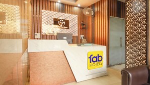 A hotel reception area with a reception desk, a clock, and a wall-mounted fan. - Fabhotel The Glory (Rishikesh)