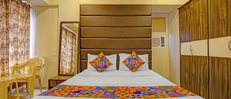 A hotel room with a large bed, a wooden wardrobe, a mirror, and a chair.