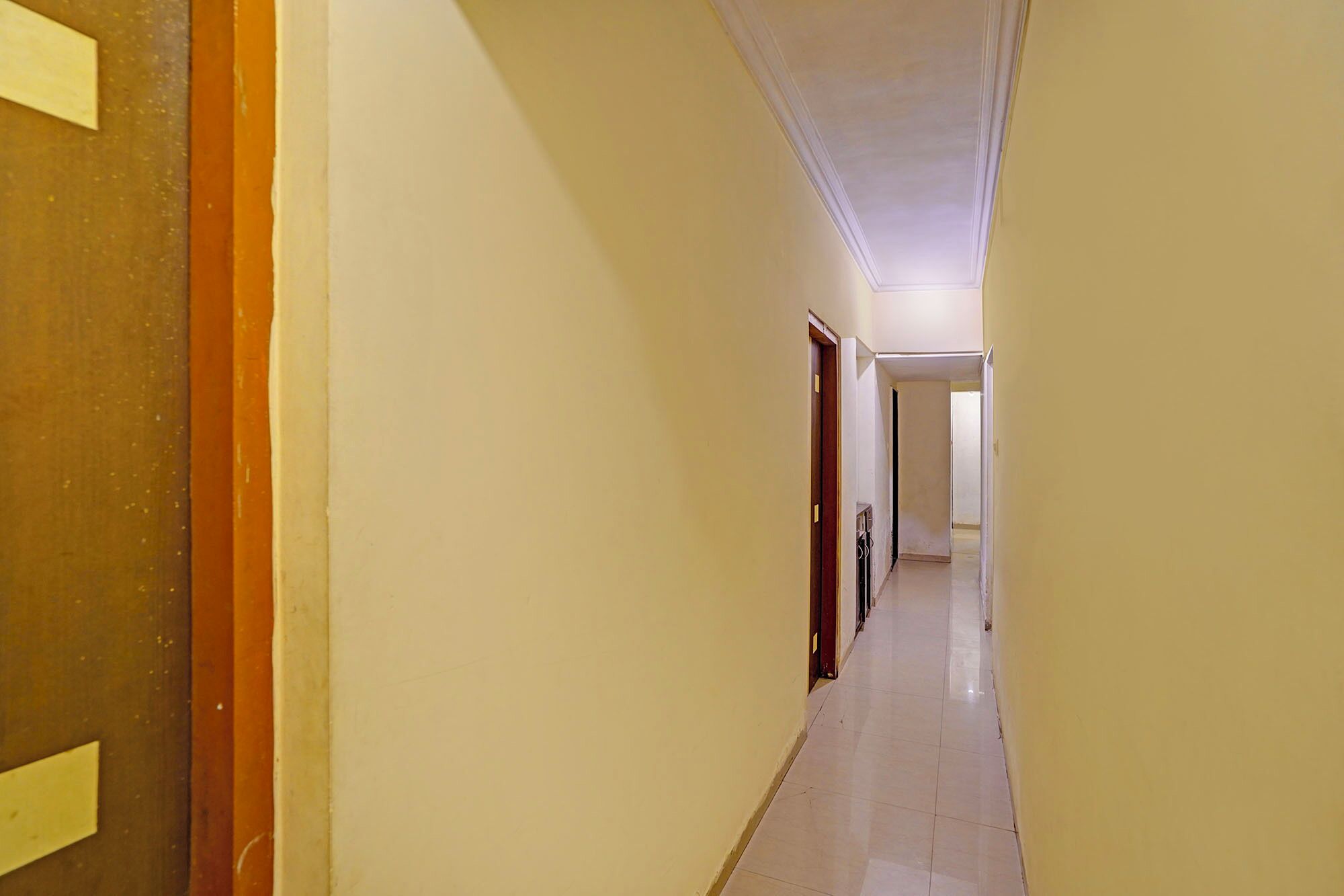 A narrow, well-lit hallway with plain walls and a tiled floor, leading to a door at the end.