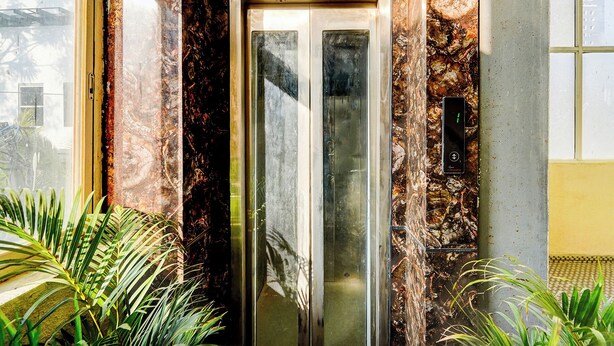 Un ascenseur avec un mur en marbre et une porte en verre, entouré de plantes.