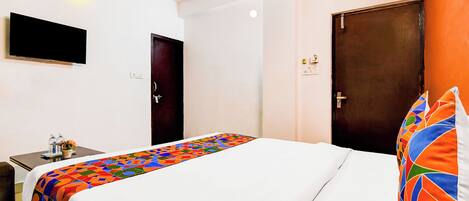 Habitación de hotel con una cama, un escritorio con silla, un televisor montado en la pared y dos puertas.