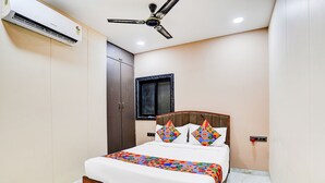 A bedroom with a bed, a ceiling fan, a wardrobe, and a window. - Fabhotel Jk (Mumbai)
