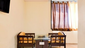 A small, well-lit room with a dining table and two chairs, a window with curtains, and a flat-screen TV mounted on the wall. - Fabhotel Park Street Inn (Ranchi)