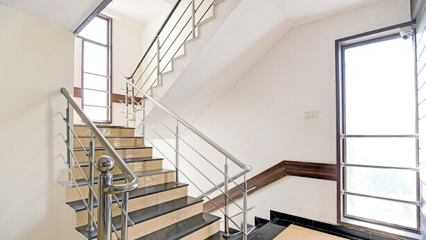 A modern staircase with metal railings and a wooden handrail, leading to a room with a large window and a door. - Fabhotel Park Street Inn (Ranchi)