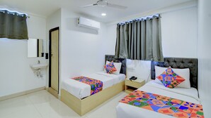 A hotel room with two beds, a small bedside table, a nightstand, a mirror, a ceiling fan, and an air conditioning unit.