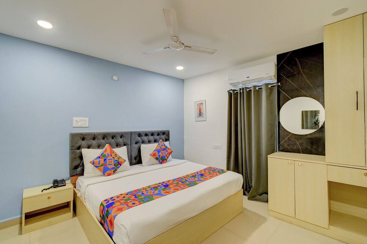 Quarto com cama, mesa de cabeceira, guarda-roupa, ventoinha no teto e ar condicionado fixado na parede.