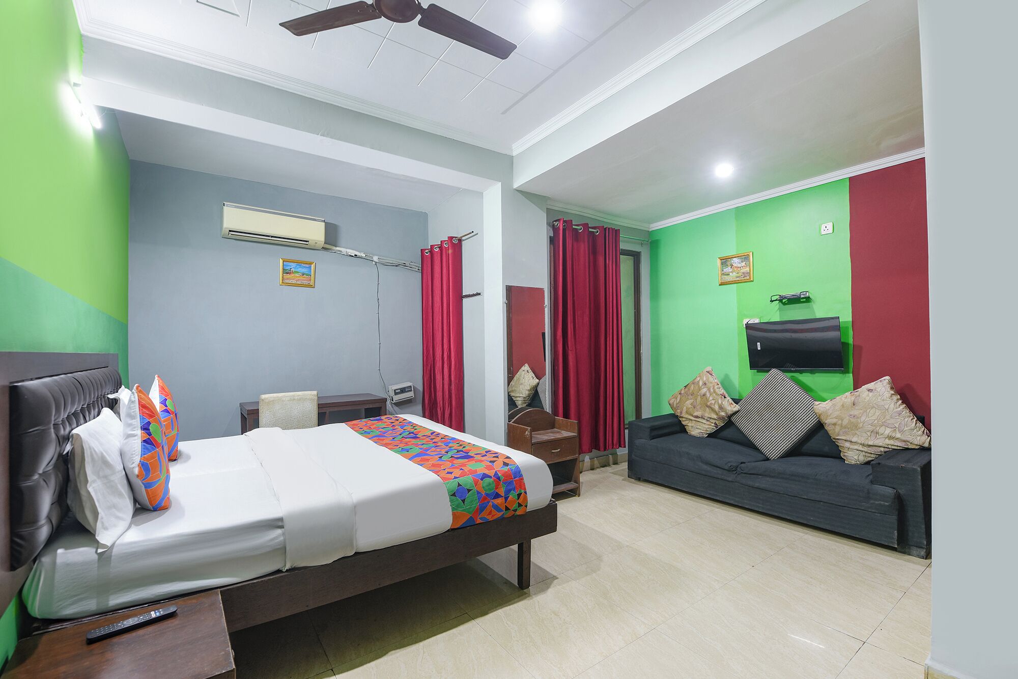 A hotel room with a bed, a sofa, a TV, and a ceiling fan.