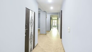 A hallway with light blue walls, a patterned door on the left, and a light-colored floor. - Via Elite Stay (Gurugram)