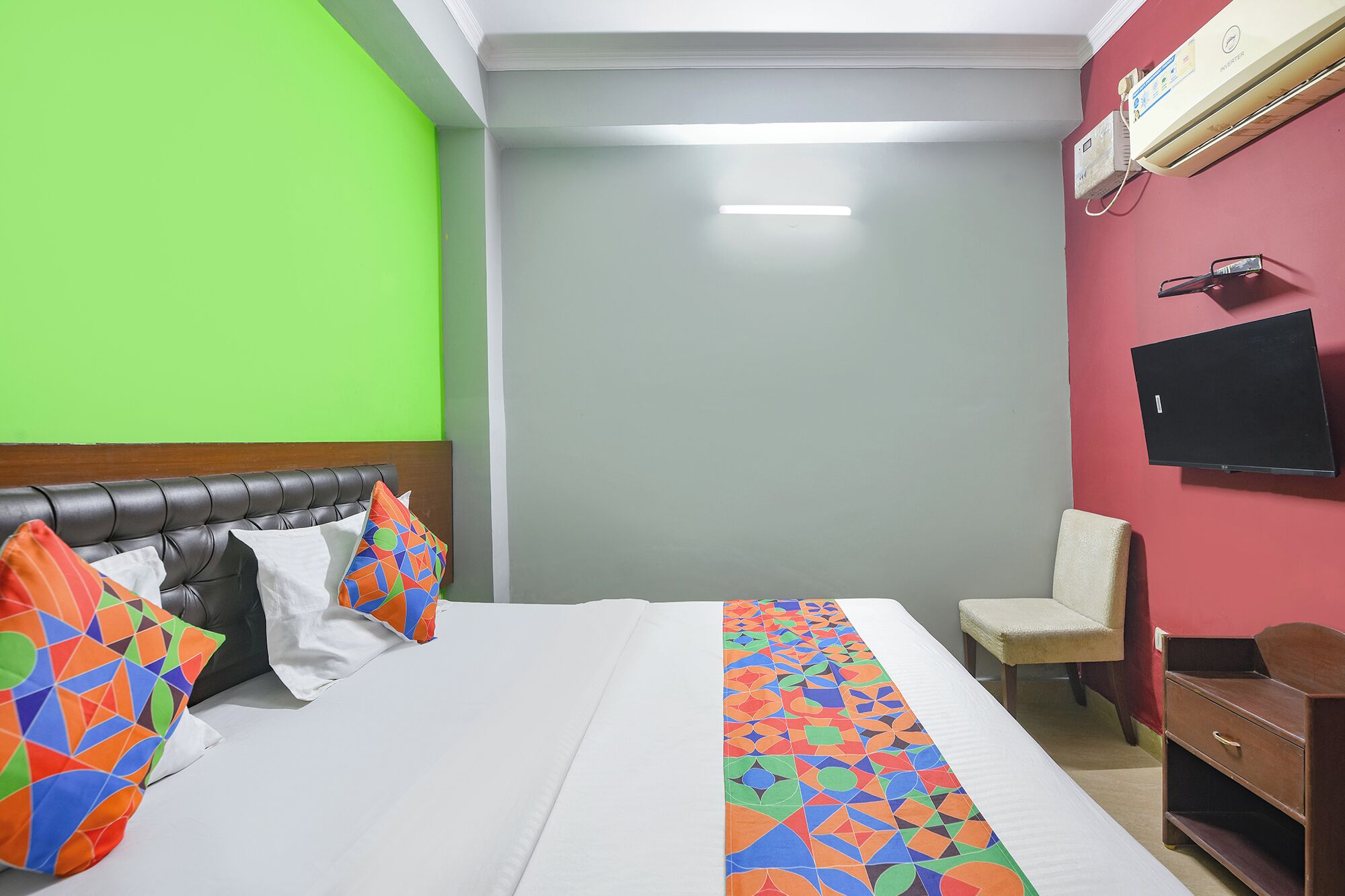 A hotel room with a bed, a chair, a desk, and a television on the wall.