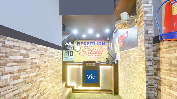A reception area with a reception desk, a clock, and a sign for Hotel Elite. - Via Elite Stay (Gurugram)