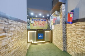 A reception area with a reception desk, a clock, a fire extinguisher, and a sign for the reception. - Via Elite Stay (Gurugram)