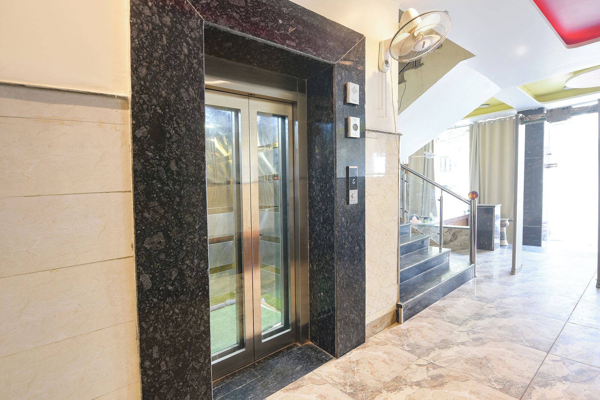 A modern elevator with glass doors, a marble floor, and a handrail.