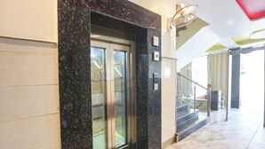A modern elevator with glass doors, a marble floor, and a handrail. - Fabhotel Dev Residency (New Delhi)