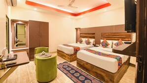 A hotel room with two beds, a green ottoman, a wooden headboard, a ceiling fan, and a TV. - Fabhotel Dev Residency (New Delhi)
