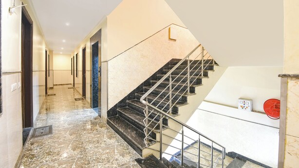 A modern hotel interior with a marble-floored corridor leading to a staircase with metal railings. - Fabhotel Dev Residency (New Delhi)