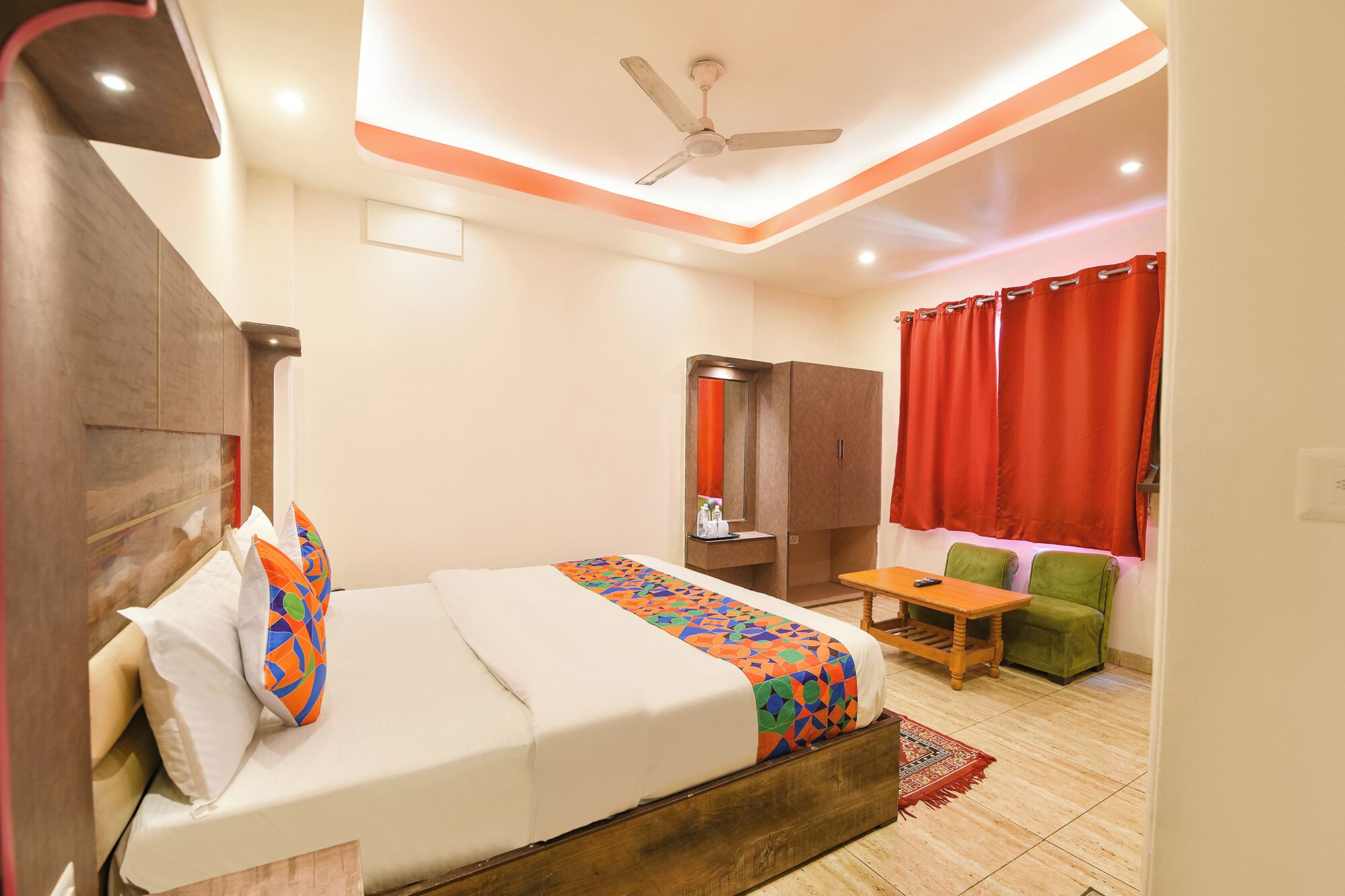 A hotel room with a bed, a desk, a chair, a wardrobe, and a red curtain.