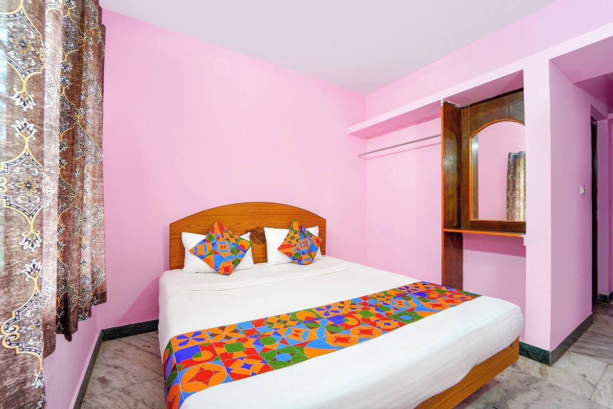 Un lit avec une couvre-lit aux motifs géométriques colorés, une tête de lit en bois et deux coussins aux motifs géométriques.
